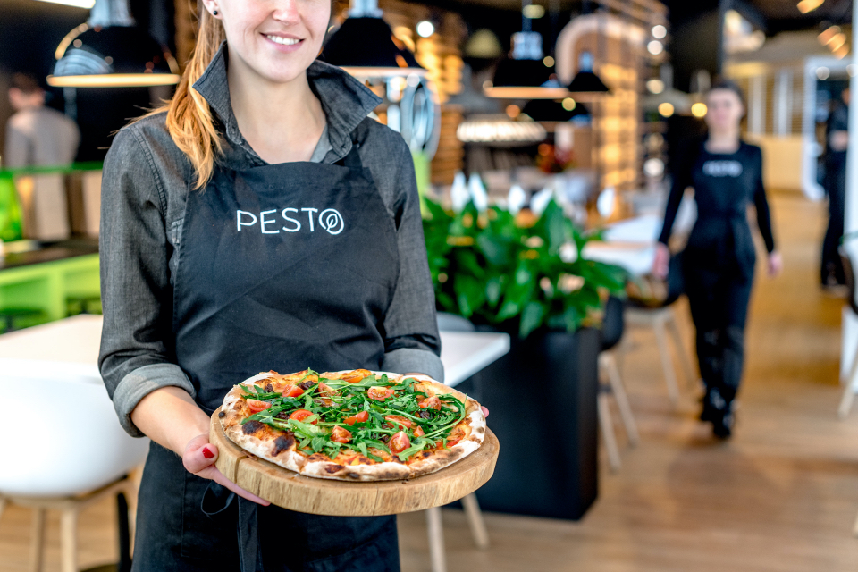 Kobieta w fartuchu Pesto trzymająca pizzę